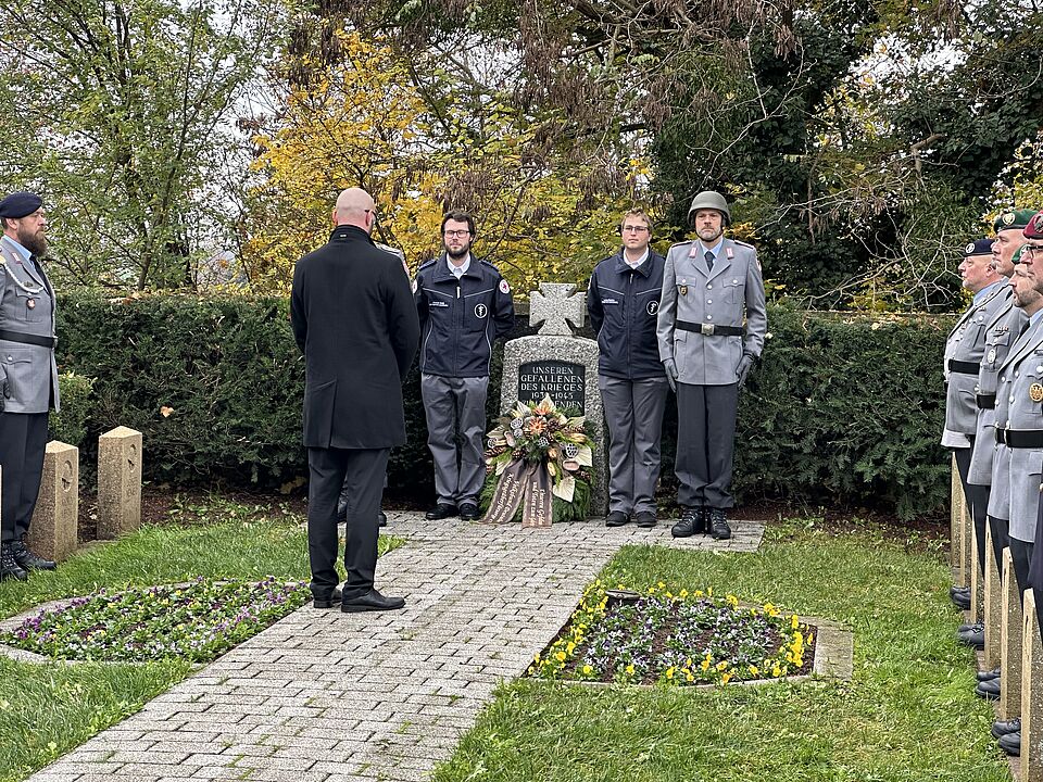 Zwei Mitglieder des DRK Ortsvereins Eggenstein-Leopoldshafen stehen jeweils links und rechts neben einem Kriegerdenkmal.